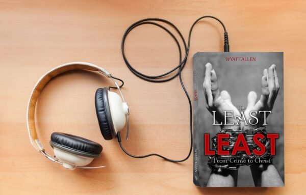 A pair of vintage-style headphones with a coiled black cord rests beside The Least of the Least (Audiobook) by Wyatt Allen, whose cover features hands in handcuffs. Both are set on a wooden surface.
